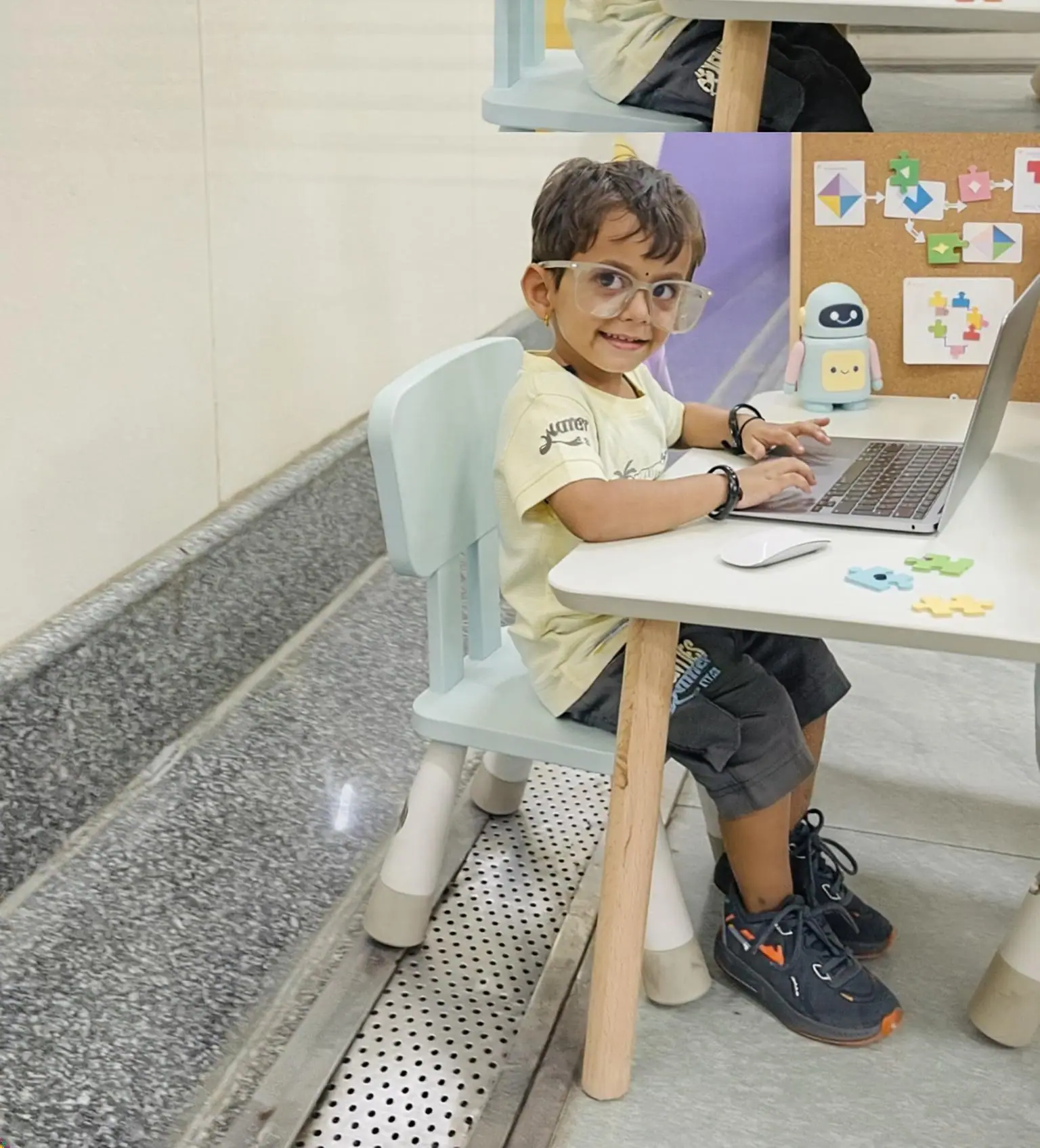 Child learning with a laptop, robot, and puzzle pieces at a desk